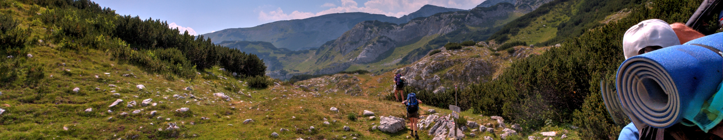 Berge und ein Tal. Pfadfinderinnen und Pfadfinder wandern mit Rucksäcken.